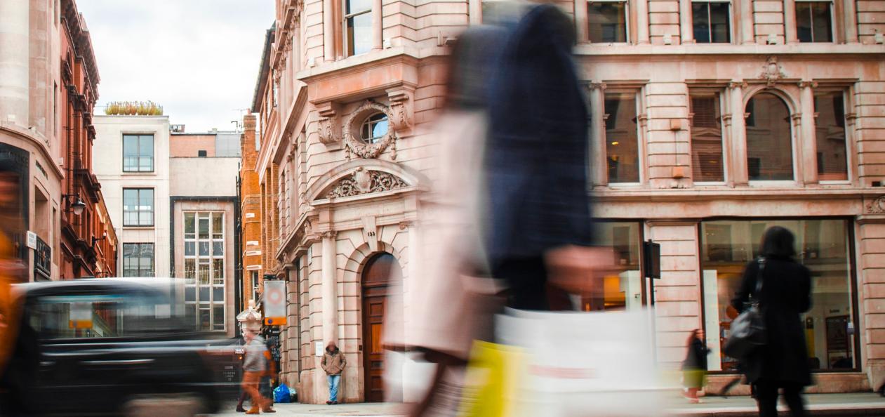 Two shoppers carrying bags outside retail stores on a city high street