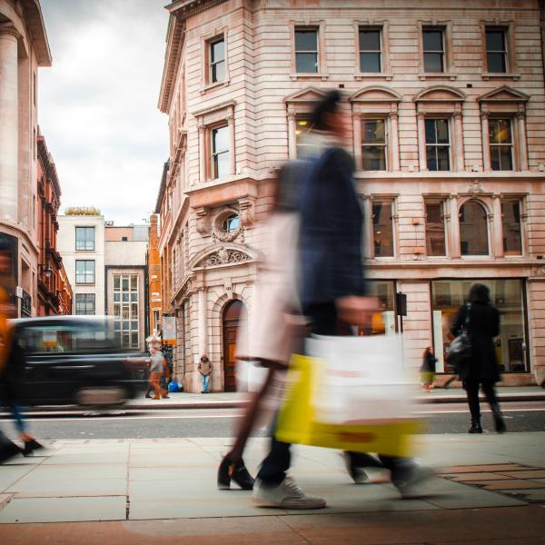 Two shoppers carrying bags outside retail stores on a city high street